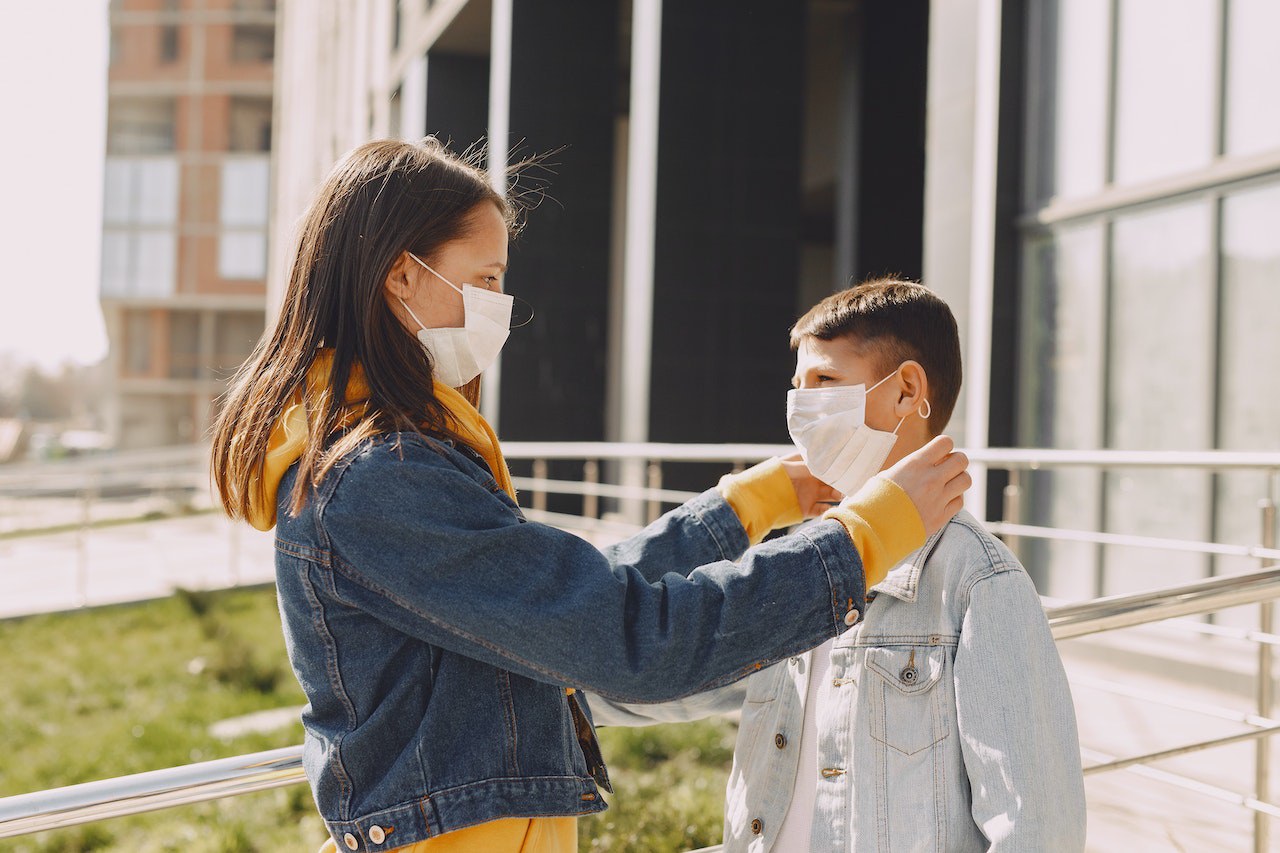 Girl in medical mask fixing medical mask on boy face